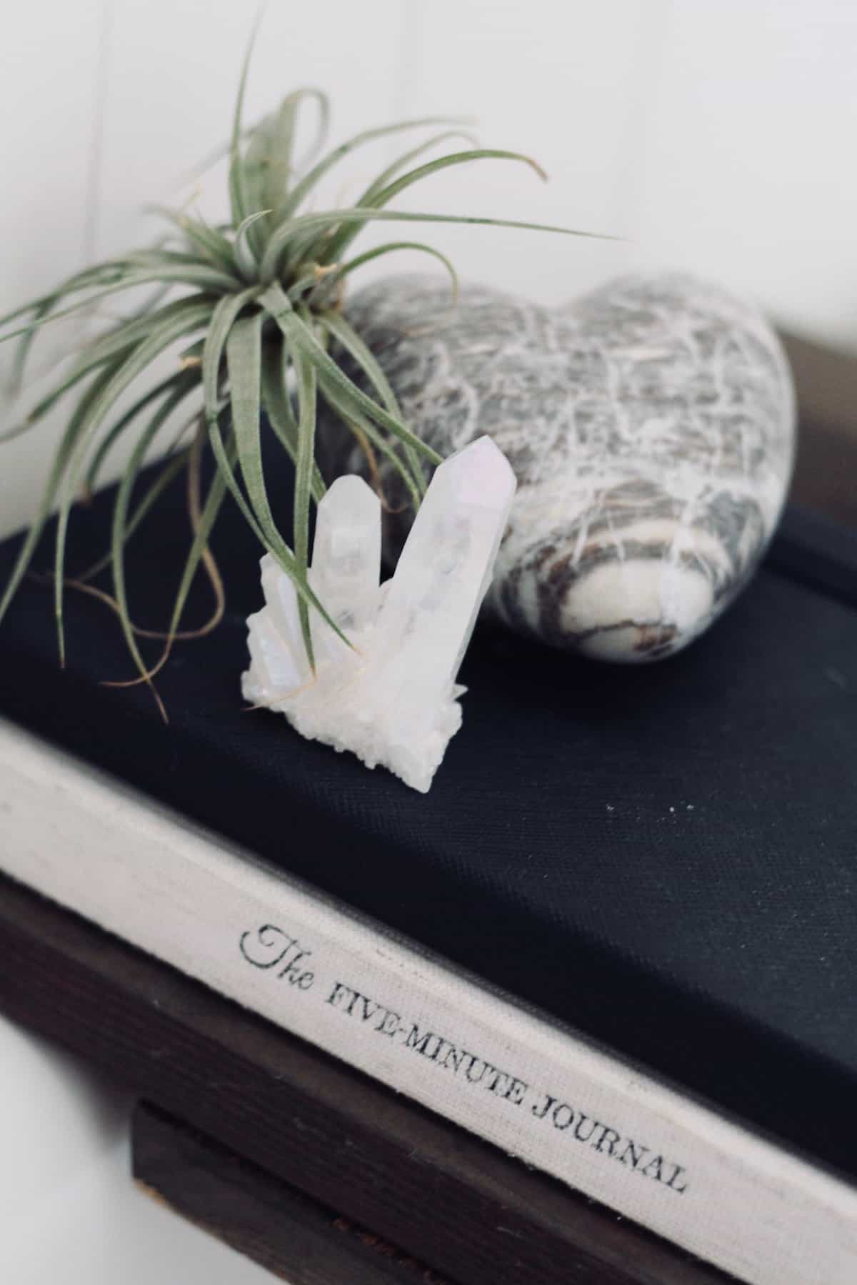 Two journals on a bath caddy topped with a green air plant, marble stone heart, and white quartz crystal for spa bathroom decor