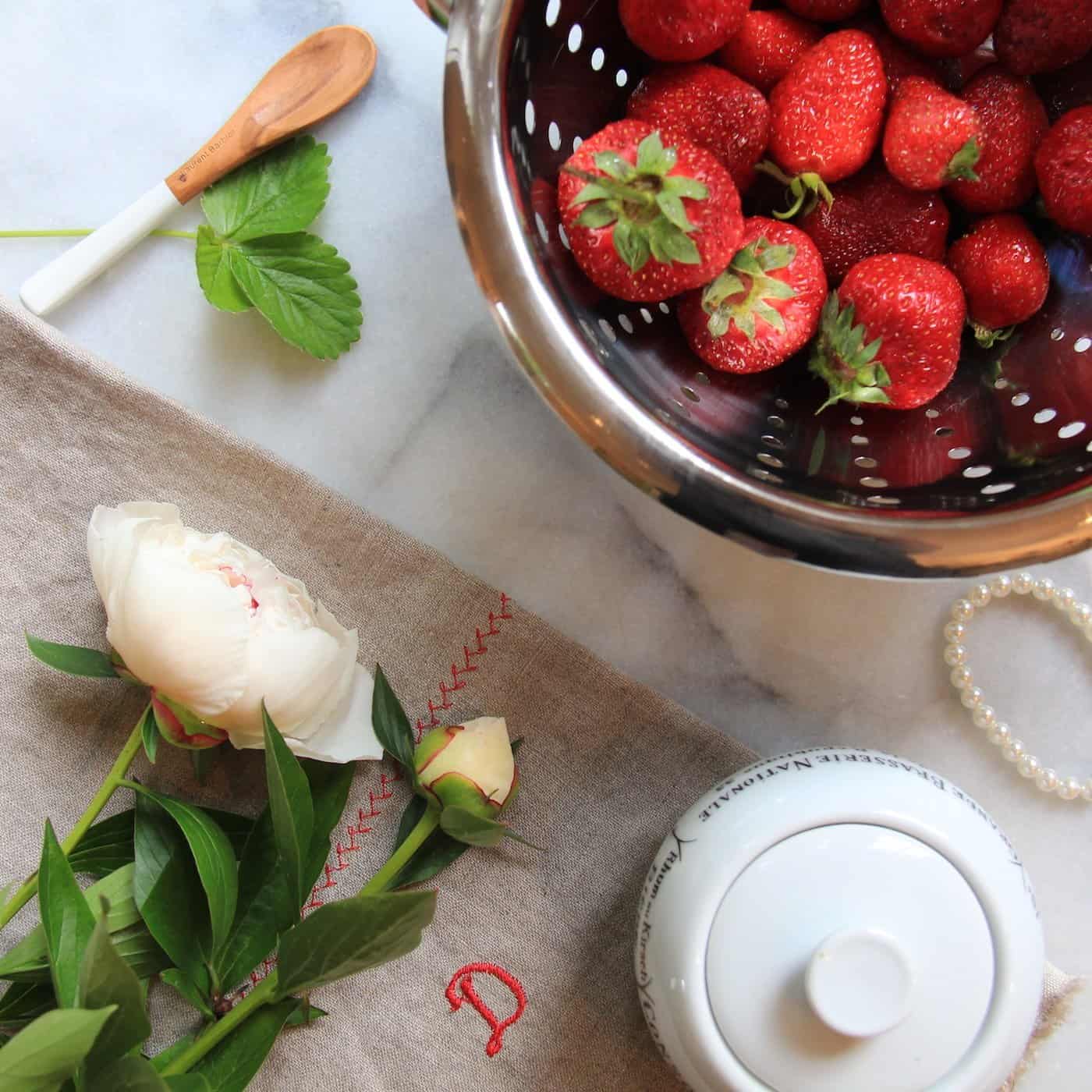 Fresh indoor strawberries in a metal colander on a marble countertop with a white peony