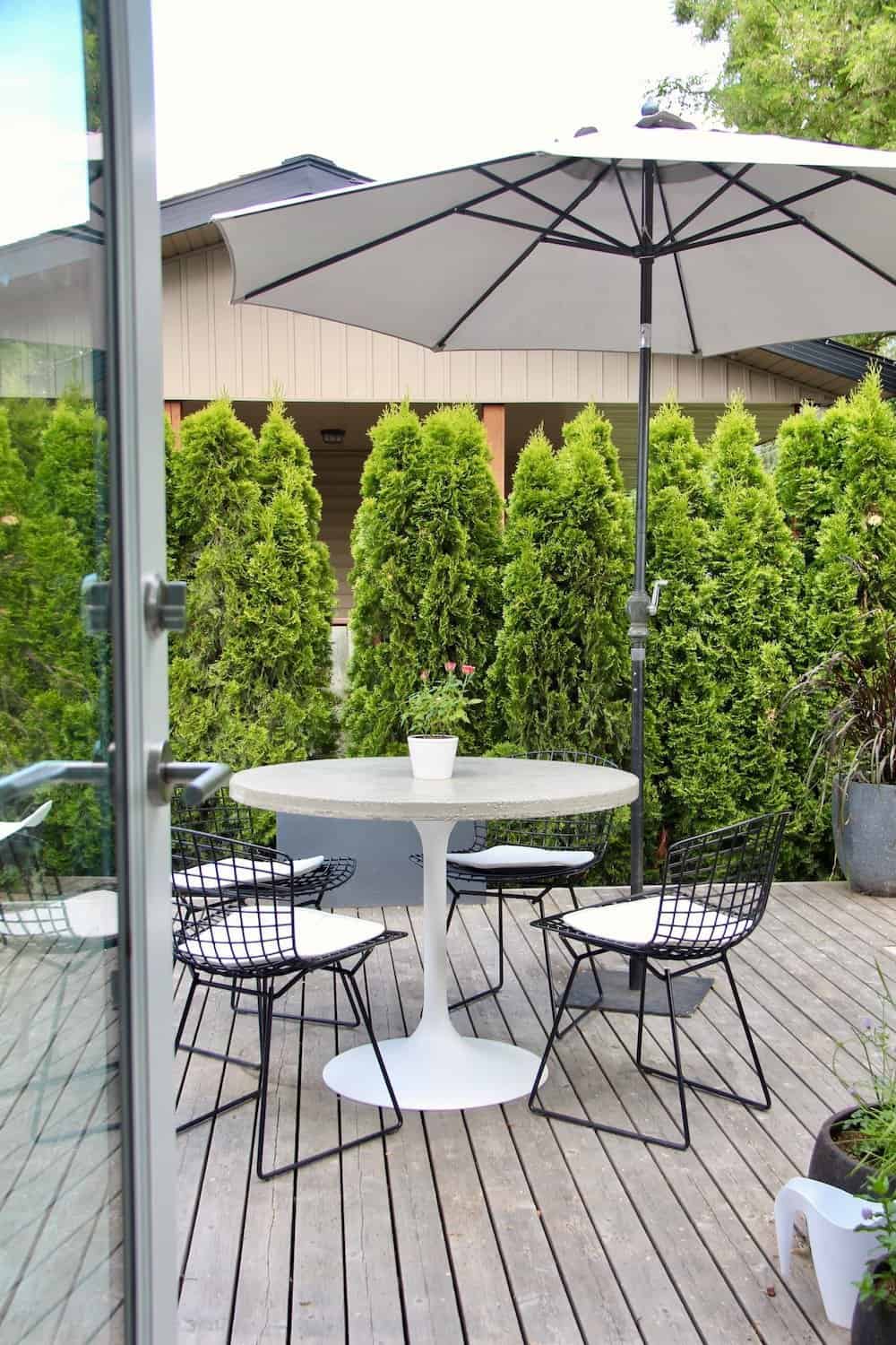 Modern patio furniture on grey wooden deck with glass door and umbrella
