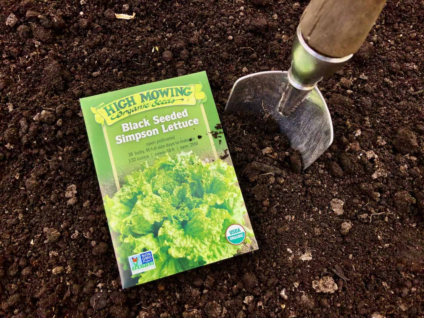 High mowing seed packet on garden soil with trowel