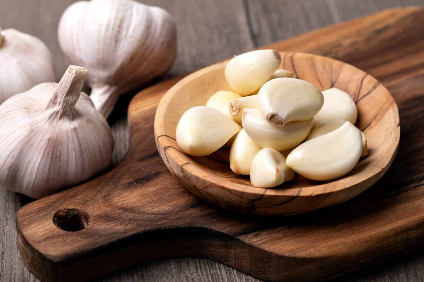 Garlic cloves in a bowl on wooden board
