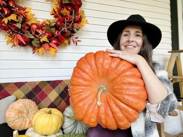 Woman holding pumpkin with other pumpkins on bench beside her